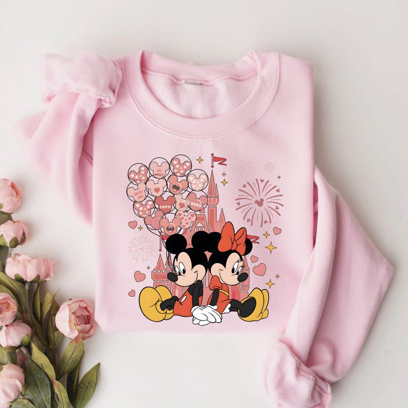 May include: Pink sweatshirt with a graphic of Mickey Mouse and Minnie Mouse in front of a pink castle with hearts and fireworks. The text "LOVE" is on one of the hearts.