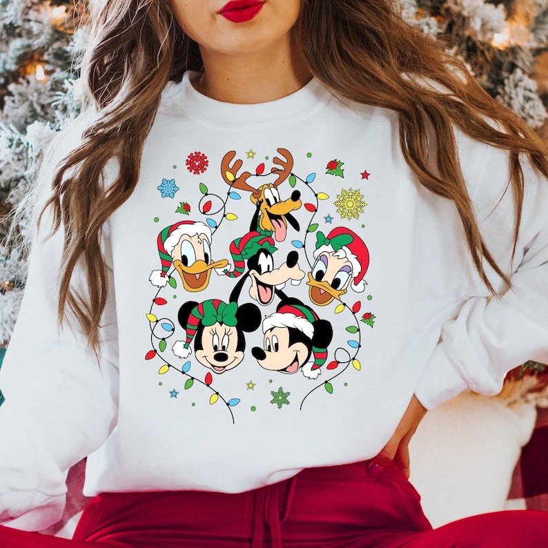 May include: White Christmas sweater with a festive design featuring Mickey Mouse, Minnie Mouse, Donald Duck, Goofy, and Pluto. The characters are surrounded by colorful Christmas lights and snowflakes.