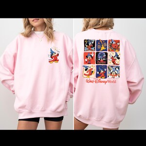 Puede incluir: Sudadera rosa con un gr&aacute;fico de Mickey Mouse en la parte delantera y un gr&aacute;fico de Mickey Mouse de varios paneles en la parte trasera. El gr&aacute;fico trasero incluye el texto "Walt Disney World".