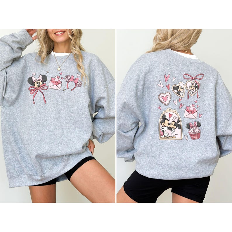 May include: A light gray sweatshirt featuring Minnie Mouse-themed graphics. The front displays Minnie with a bow, hearts, and a bow-shaped headband. The back showcases Minnie and Mickey Mouse with hearts and a cupcake.