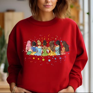 May include: Red sweatshirt with a graphic of seven princesses standing back to back with stars around them.