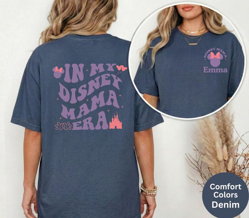 Puede incluir: Camisetas azul denim con gr&aacute;ficos tem&aacute;ticos de Disney. Una camiseta presenta "IN MY DISNEY MAMA ERA" en morado y rosa. La otra camiseta tiene "DISNEY MAMA" con un lazo y el nombre "Emma".