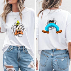 K&ouml;nnte beinhalten: Wei&szlig;es T-Shirt mit einem Cartoon-Charakter-Design. Die Vorderseite zeigt das Gesicht der Figur, das aus einem zerrissenen Loch kommt, und die R&uuml;ckseite zeigt die Beine und F&uuml;&szlig;e der Figur. Das Design enth&auml;lt orange, gelbe und blaue Akzente.