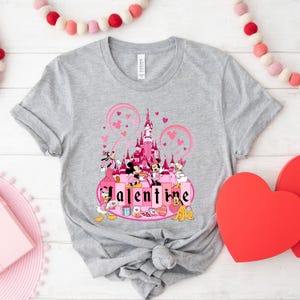 May include: A gray t-shirt with a pink and white graphic of Mickey Mouse and friends in front of a pink castle with the word "Valentine" printed below.