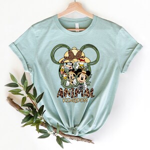 May include: A light blue t-shirt with a graphic of Mickey Mouse and friends in a jungle setting. The graphic includes the text "Animal Kingdom".