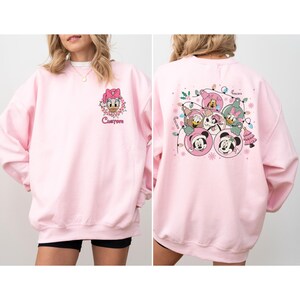May include: A light pink sweatshirt featuring a Daisy Duck graphic on the front and a group of Disney characters on the back. The front graphic includes the word "Custom". The back graphic includes Mickey Mouse, Minnie Mouse, Donald Duck, Daisy Duck, and Goofy.