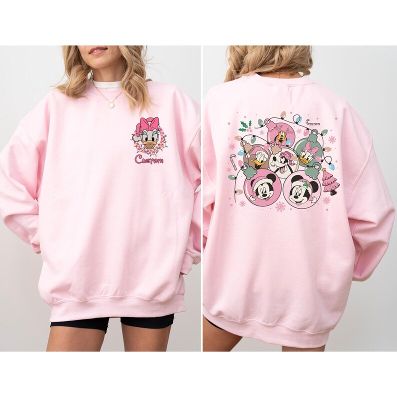 May include: A light pink sweatshirt featuring a Daisy Duck graphic on the front and a group of Disney characters on the back. The front graphic includes the word "Custom". The back graphic includes Mickey Mouse, Minnie Mouse, Donald Duck, Daisy Duck, and Goofy.