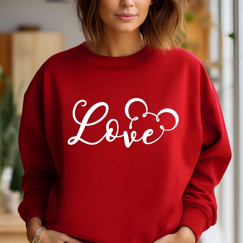 K&ouml;nnte beinhalten: Roter Pullover mit einem wei&szlig;en Aufdruck des Wortes "Love" mit einem stilisierten Mickey-Mouse-Ohren-Design.