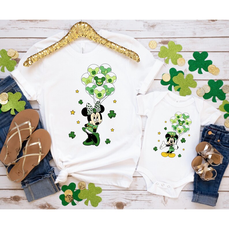 May include: A white t-shirt and a white bodysuit with a green shamrock and a cartoon mouse holding green balloons. The mouse is wearing a green hat and a green dress.