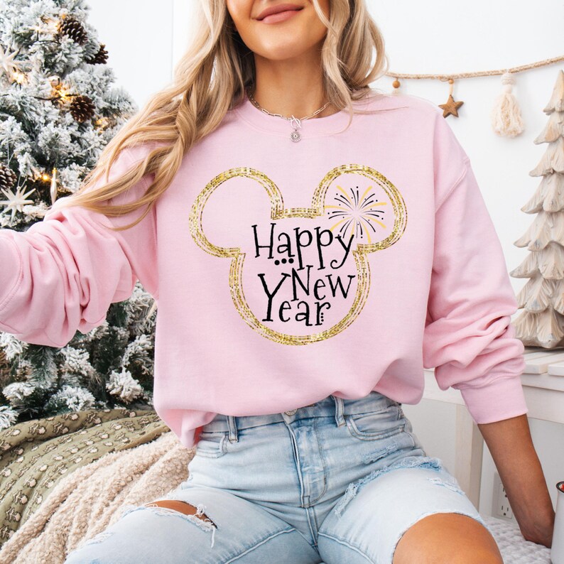 May include: A pink sweatshirt with a gold glitter Mickey Mouse head design and the text "Happy New Year" in black.
