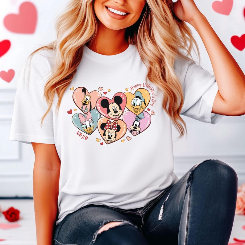 Puede incluir: Camiseta blanca con un gr&aacute;fico de Mickey Mouse, Minnie Mouse, Donald Duck, Goofy y Pluto en corazones. El texto "Happy Valentine's Day" y "XOXO" tambi&eacute;n est&aacute;n en la camiseta.