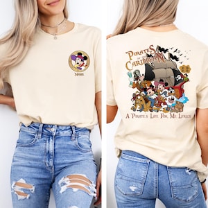 May include: A beige t-shirt with a graphic of Mickey Mouse dressed as a pirate on the front and a graphic of Mickey Mouse and other Disney characters on a pirate ship with the text "Pirates of the Caribbean" and "A Pirate's Life For Me Lyrics" on the back.