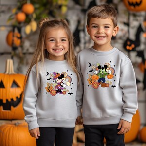 K&ouml;nnte beinhalten: Zwei hellgraue Sweatshirts mit Halloween-Cartoonfiguren. Eines zeigt Minnie Mouse mit Hexenhut, das andere Mickey Mouse mit K&uuml;rbissen. Beide haben farbenfrohe Grafiken, ideal f&uuml;r die gruselige Jahreszeit. Ma&szlig;e sind nicht verf&uuml;gbar.