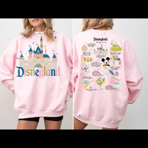 May include: Pink sweatshirt with a graphic print of Disneyland's Sleeping Beauty Castle on the front and a map of Disneyland attractions on the back. The text "Disneyland" is printed in large letters on the front of the sweatshirt.