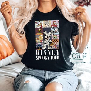 Pu&ograve; includere: T-shirt nero con una griglia di personaggi Disney in costume di Halloween. Il design include Paperino, Topolino e Stitch. Il testo "DISNEY SPOOKY TOUR" &egrave; stampato in bianco sotto la griglia.
