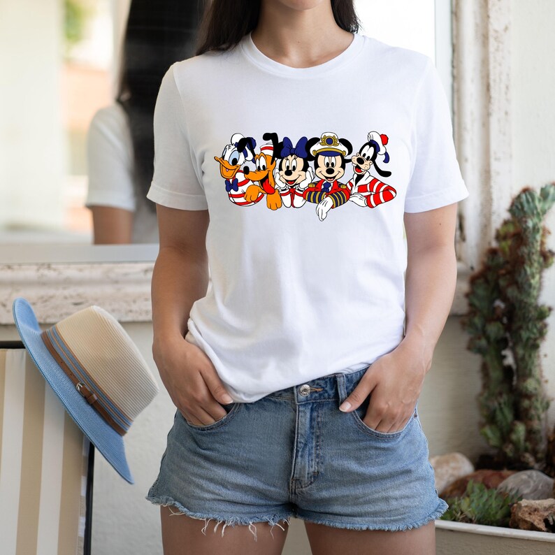 Peut inclure: T-shirt blanc avec un motif de Mickey Mouse, Donald Duck, Dingo et Pluto portant des tenues de marin. Les personnages sourient et saluent.