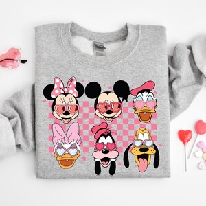 May include: Gray sweatshirt with a pink and white checkered background featuring Mickey Mouse, Minnie Mouse, Donald Duck, Goofy, and Pluto wearing heart-shaped sunglasses.