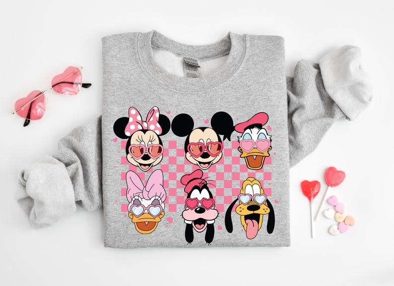May include: Gray sweatshirt with a pink and white checkered background featuring Mickey Mouse, Minnie Mouse, Donald Duck, Goofy, and Pluto wearing heart-shaped sunglasses.