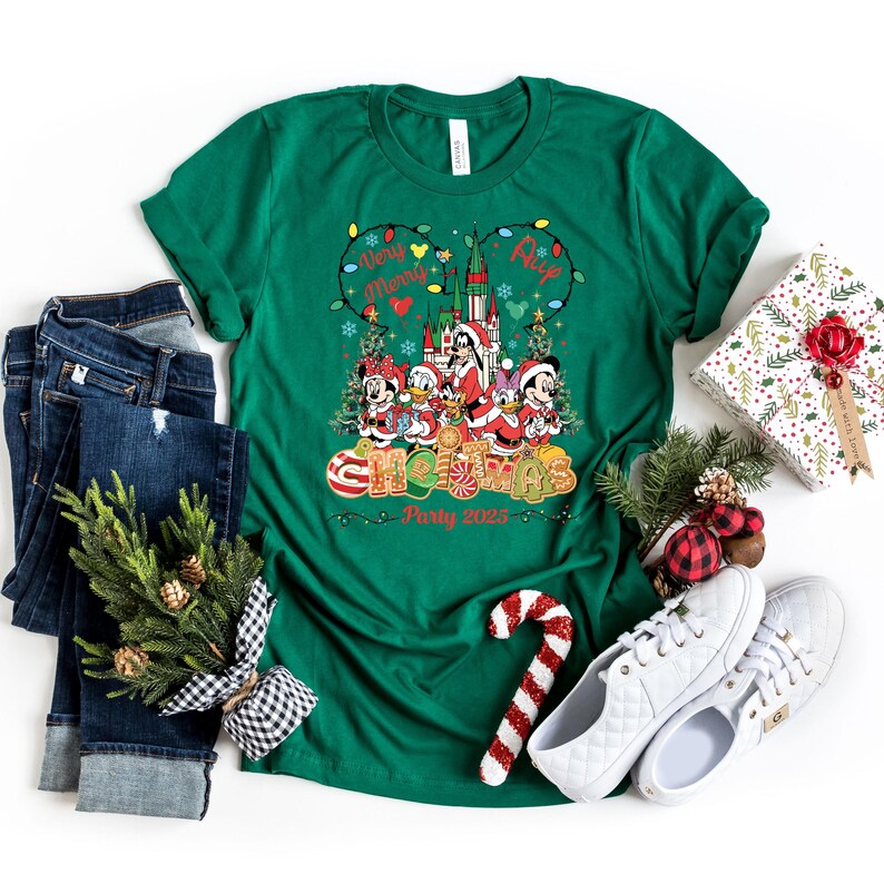 May include: Green Christmas-themed t-shirt with a graphic featuring Disney characters in Santa outfits, a castle, and the words "Very Merry Christmas Party 2023." The shirt is paired with jeans, sneakers, and a wrapped gift.