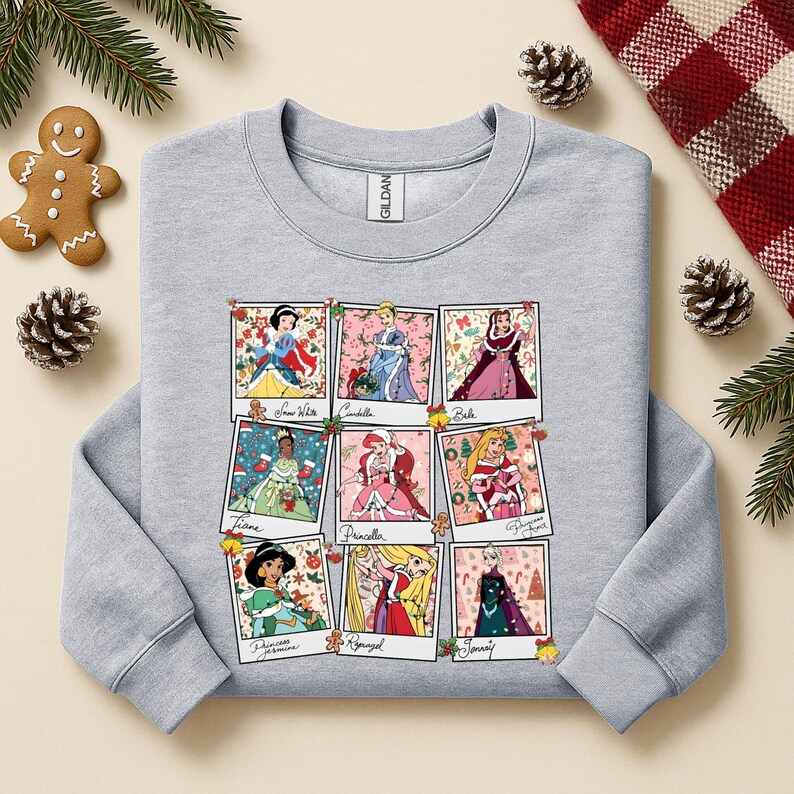 Puede incluir: Una sudadera gris claro con una cuadr&iacute;cula de nueve retratos de princesas de Disney en marcos estilo polaroid. Cada marco tiene un hombre de jengibre y decoraciones navide&ntilde;as. Las princesas son Blancanieves, Cenicienta, Bella, Tiana, Ariel, Aurora, Jasmine, Rapunzel y Elsa.