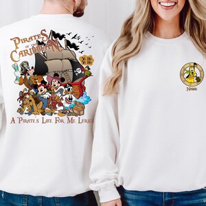 May include: White sweatshirt with a colorful cartoon image of Mickey Mouse and friends on a pirate ship. The text "Pirates of the Caribbean" and "A Pirate's Life For Me Lyrics" are printed on the sweatshirt.