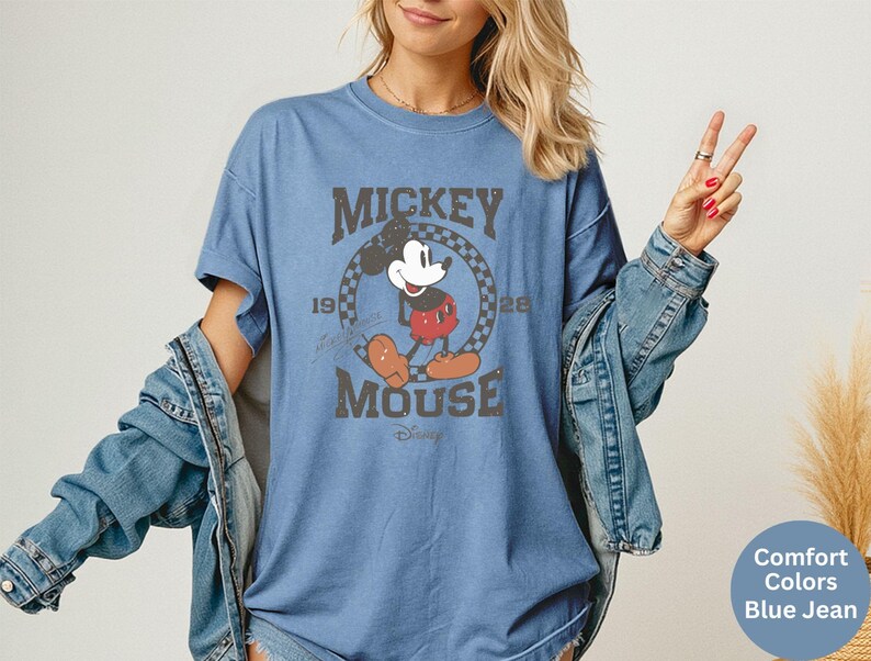 May include: Blue t-shirt featuring a distressed graphic of Mickey Mouse with the text "Mickey Mouse 1928". The shirt is a comfort color blue jean. The shirt is a short-sleeved, crew neck style.