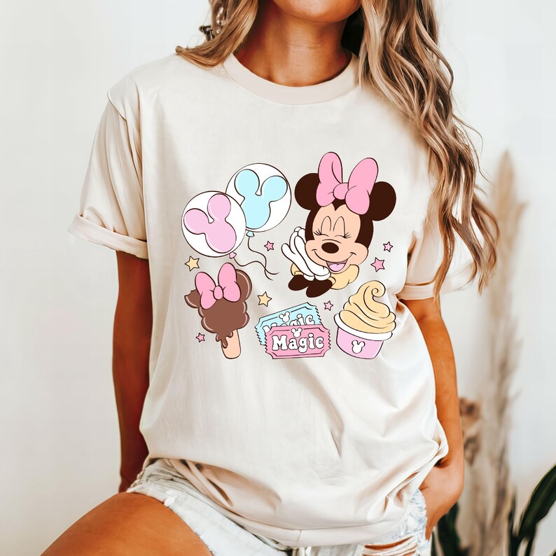 May include: A beige t-shirt with a cartoon image of Minnie Mouse holding a Mickey Mouse balloon. The design also includes a Mickey Mouse ice cream cone, a Mickey Mouse ice cream bar, and a ticket that says "Walt Disney World Magic".