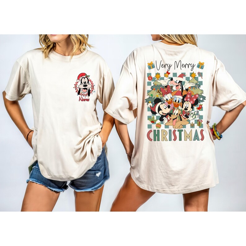 May include: Beige t-shirt featuring a front graphic of Goofy in a Santa hat and the name "Nurse". The back of the shirt displays a "Very Merry Christmas" design with Disney characters, Christmas trees, and gift boxes. The word "CHRISTMAS" is printed at the bottom.