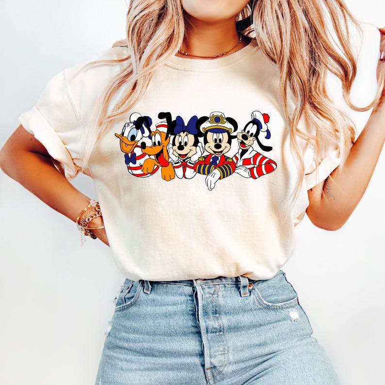 Peut inclure: Un t-shirt blanc avec un imprim&eacute; graphique de Mickey Mouse, Minnie Mouse, Donald Duck, Dingo et Pluto portant des tenues de marin. Les personnages sont tous souriants et ont des accents rouge, blanc et bleu.