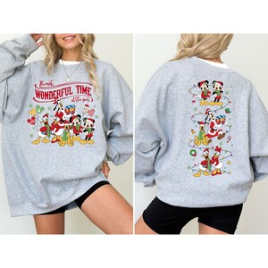 May include: A light gray sweatshirt featuring a festive Disney design. The front displays Mickey, Minnie, Donald, and Goofy in holiday attire with the text "The most WONDERFUL TIME of the year." The back has a vertical design of Disney characters.