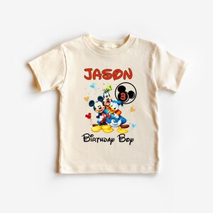 May include: Cream-colored t-shirt featuring Mickey Mouse, Donald Duck, and Goofy. The shirt has the name "JASON" in red, the number "3", and the words "Birthday Boy" in black. The design includes colorful confetti.