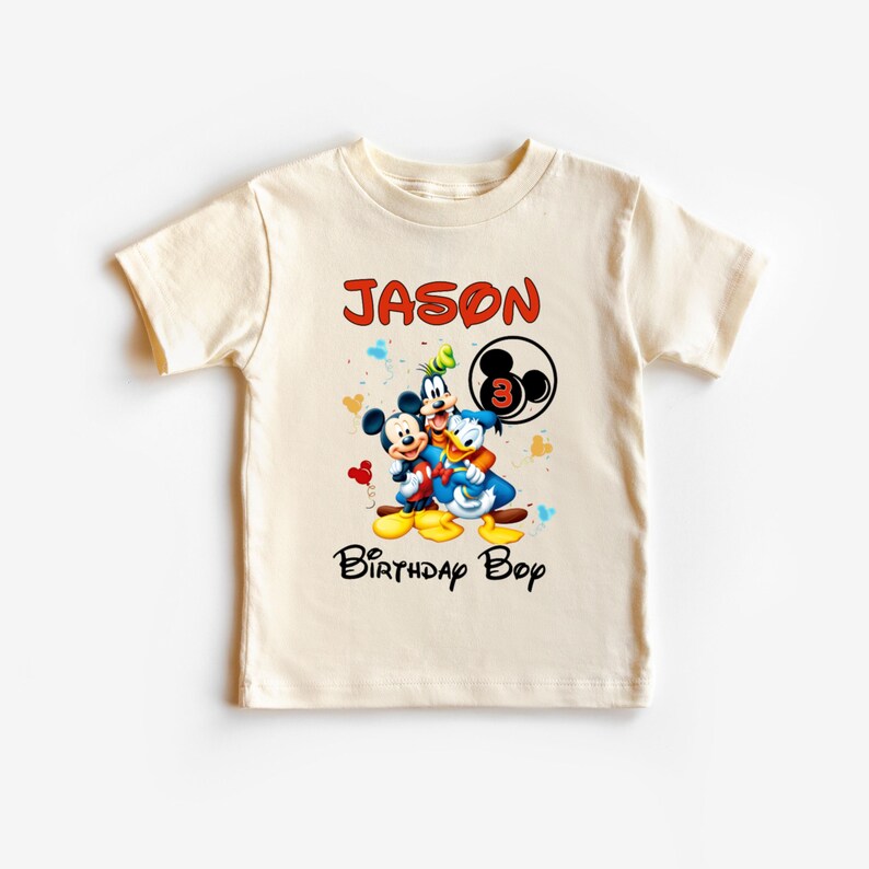 May include: Cream-colored t-shirt featuring Mickey Mouse, Donald Duck, and Goofy. The shirt has the name "JASON" in red, the number "3", and the words "Birthday Boy" in black. The design includes colorful confetti.