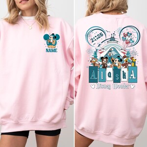 May include: Pink sweatshirt with a Mickey Mouse design on the front and a Mickey Mouse design with the text "Alaska" and "Disney Wonder" on the back.