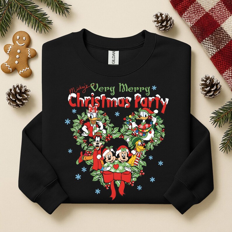 Op de afbeelding: Zwarte sweatshirt met een kerstontwerp met Mickey Mouse en vrienden. De tekst "Mickey's Very Merry Christmas Party" staat boven de krans. Het ontwerp bevat rood, groen en wit.