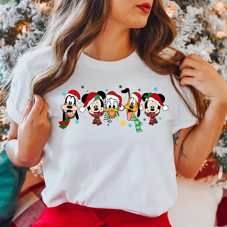 May include: White t-shirt with a Christmas-themed design featuring Mickey Mouse, Minnie Mouse, Donald Duck, Goofy, and Pluto wearing Santa hats and scarves.