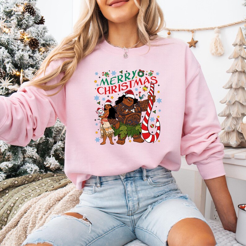 May include: A light pink sweatshirt featuring a graphic of two cartoon characters with Santa hats and a candy cane. The words "MERRY CHRISTMAS" are above the characters in green and red. The sweatshirt is a long-sleeved crew neck.