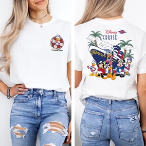 以下が含まれることがあります： ディズニー・クルーズのデザインが施された白いTシャツ。Tシャツの前身頃には、ライフジャケットを着たドナルドダックの漫画の画像が描かれています。Tシャツの後ろ身頃には、ディズニー・クルーズの船の前に立っているミッキーマウス、ミニーマウス、ドナルドダック、グーフィー、プルートの漫画の画像が描かれています。Tシャツの後ろ身頃には、「ディズニー・クルーズ」の文字が印刷されています。