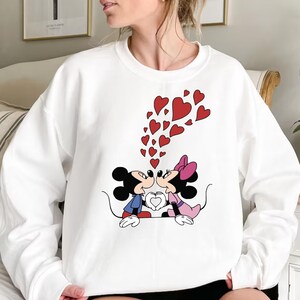 May include: White sweatshirt with a graphic of Mickey Mouse and Minnie Mouse kissing with red hearts floating around them.