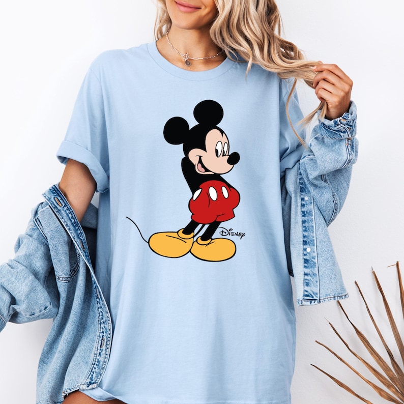 K&ouml;nnte beinhalten: Ein hellblaues T-Shirt mit einem Aufdruck von Mickey Mouse in einem roten und schwarzen Outfit. Der Text "Disney" ist unter Mickey Mouse gedruckt.