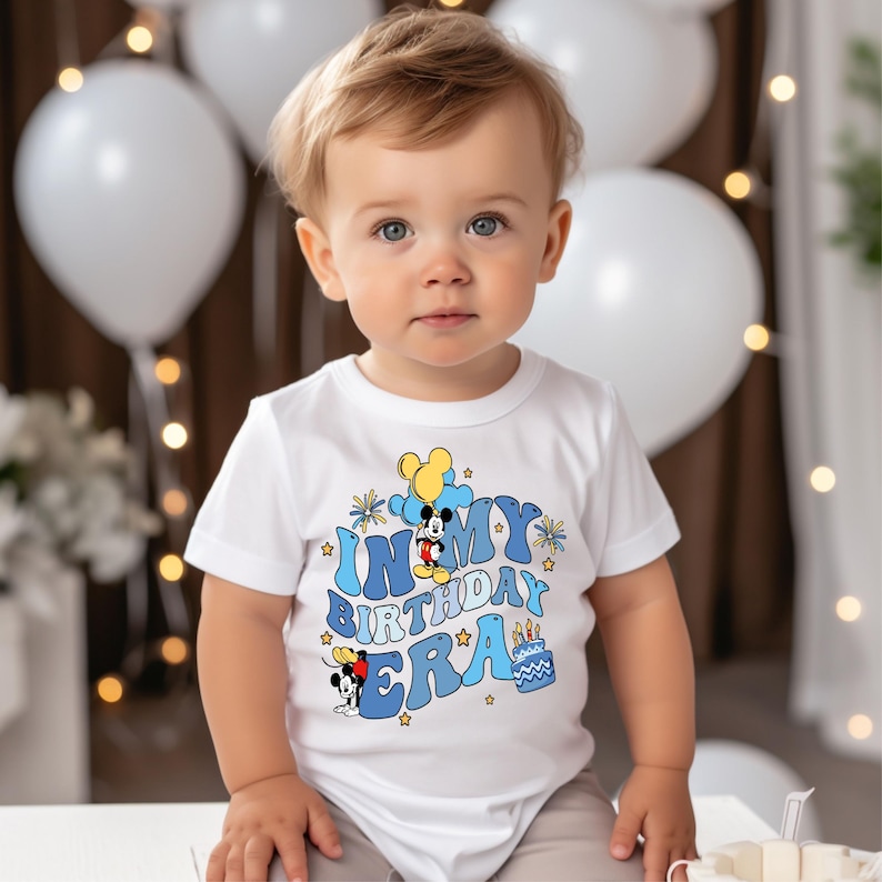 May include: A white t-shirt with a blue and yellow graphic of Mickey Mouse and the text "In My Birthday Era".