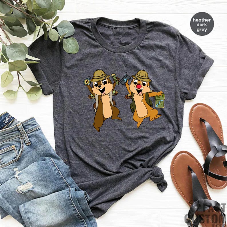 May include: A heather dark grey t-shirt featuring a graphic of two chipmunks wearing explorer hats and holding maps and compasses. The chipmunks are brown with white accents and red noses.