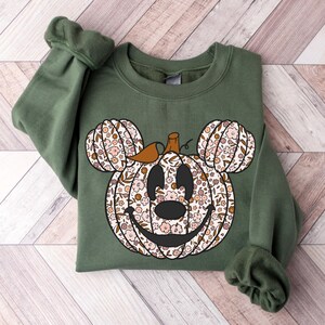 May include: A green sweatshirt with a floral pumpkin design in the shape of Mickey Mouse's head.