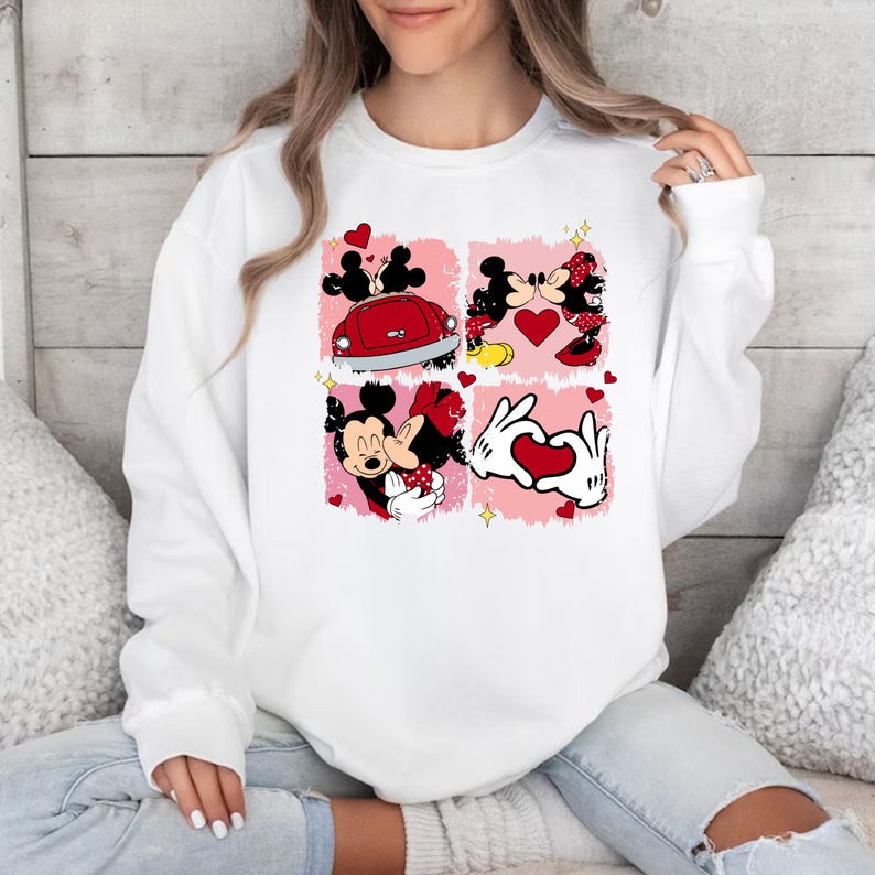 May include: White sweatshirt featuring a graphic print of Mickey Mouse and Minnie Mouse in four different scenes. The scenes include Mickey and Minnie kissing, Mickey and Minnie driving a red car, Mickey and Minnie hugging, and Mickey and Minnie making a heart shape with their hands.