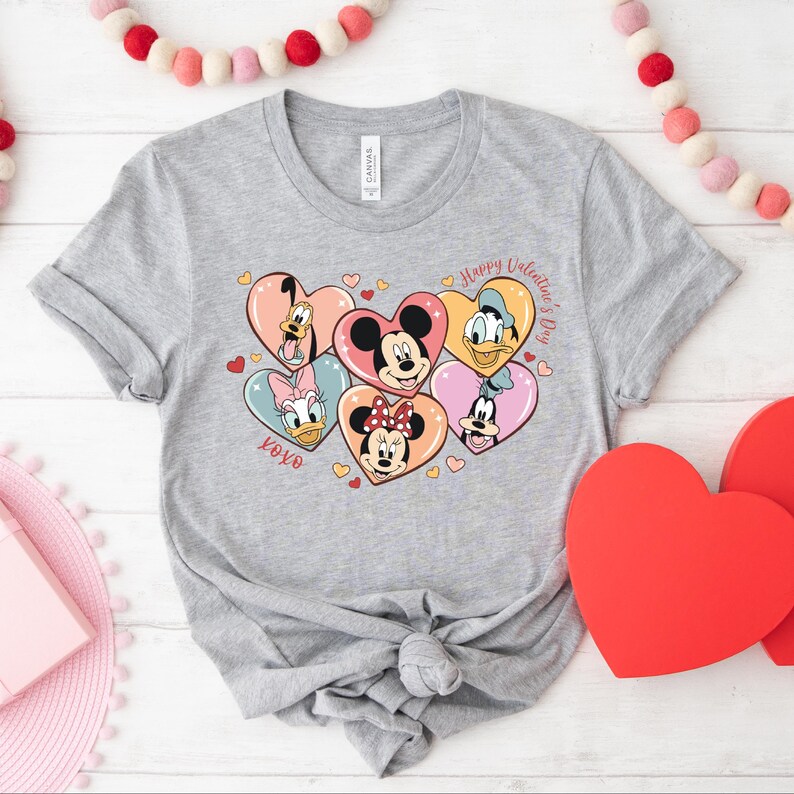 Puede incluir: Camiseta gris con un gr&aacute;fico de Mickey Mouse, Minnie Mouse, Donald Duck, Goofy y Pluto en corazones. El texto "Happy Valentine's Day" y "XOXO" tambi&eacute;n est&aacute;n en la camiseta.