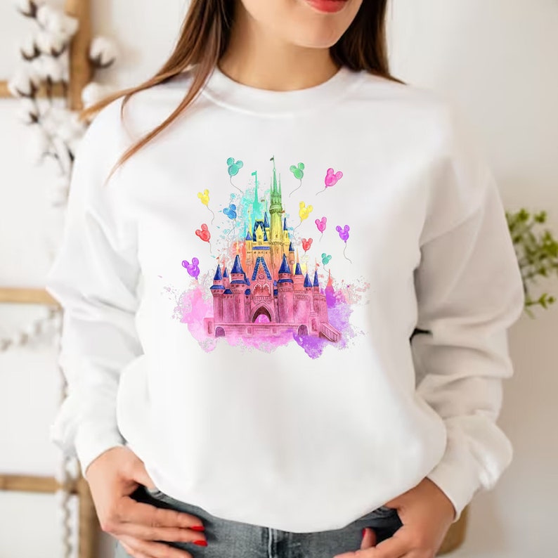 May include: A white sweatshirt with a colorful watercolor illustration of Cinderella's castle with Mickey Mouse balloons.