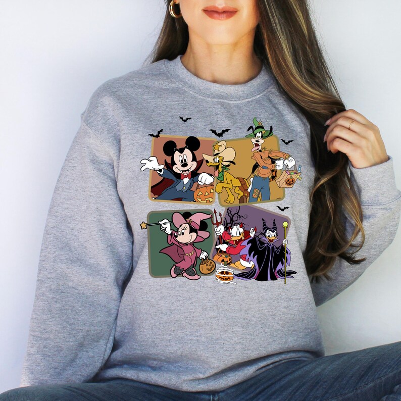 K&ouml;nnte beinhalten: Ein graues Sweatshirt mit einem bunten Aufdruck von Mickey Mouse und anderen Disney-Charakteren, die in Halloween-Kost&uuml;men gekleidet sind. Die Figuren halten K&uuml;rbisse und S&uuml;&szlig;igkeiten. Der Druck ist von Flederm&auml;usen umgeben.