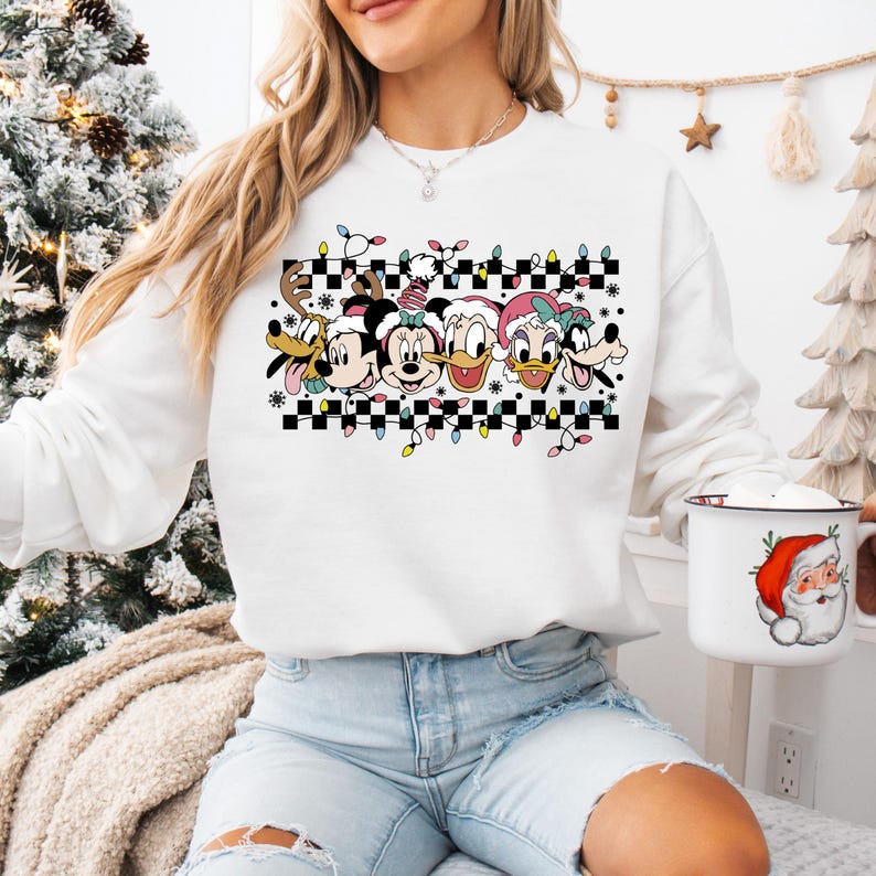 May include: White Christmas sweatshirt with a black and white checkered pattern and a row of cartoon characters wearing Santa hats. The characters include Mickey Mouse, Minnie Mouse, Donald Duck, Daisy Duck, and Pluto.