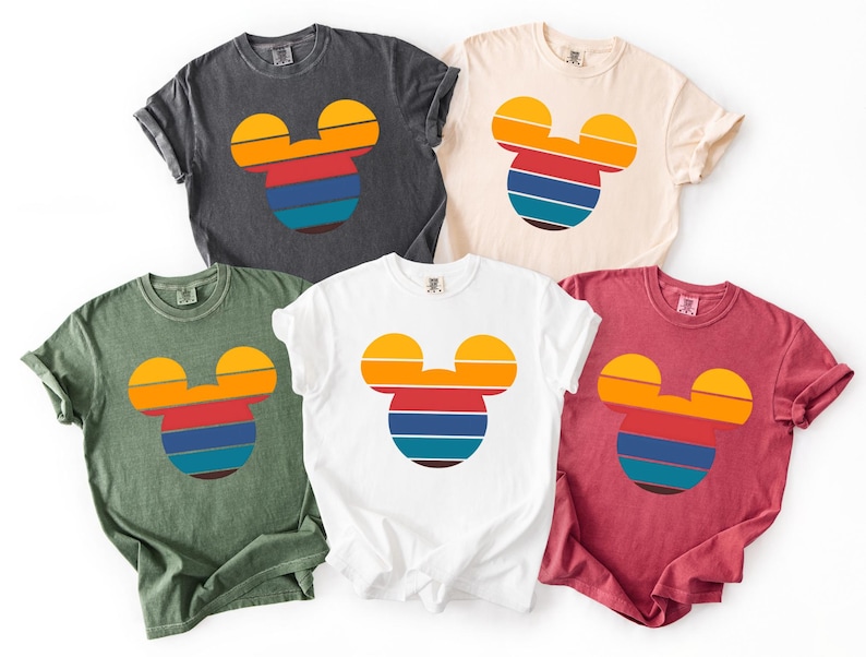 K&ouml;nnte beinhalten: F&uuml;nf T-Shirts in verschiedenen Farben: Anthrazit, Creme, Wei&szlig;, Gr&uuml;n und Weinrot. Jedes Shirt hat ein Retro-Mickey-Mouse-Kopf-Design mit horizontalen Streifen in Orange, Gelb, Rot, Blau und T&uuml;rkis.