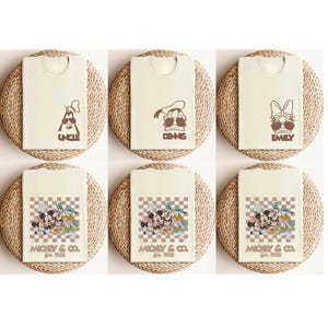 May include: Cream-colored t-shirts with brown graphics of Disney characters and names. The top row features "UNCLE", "DENNIS", and "EMILY". The bottom row displays a group graphic with "MICKEY & CO. Est. 1928".