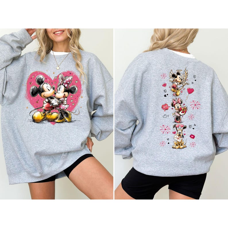 May include: A gray sweatshirt featuring a large pink heart with Mickey and Minnie Mouse embracing. The back of the sweatshirt has a vertical design with Mickey, Minnie, Pluto, and hearts. The sweatshirt has a white collar.
